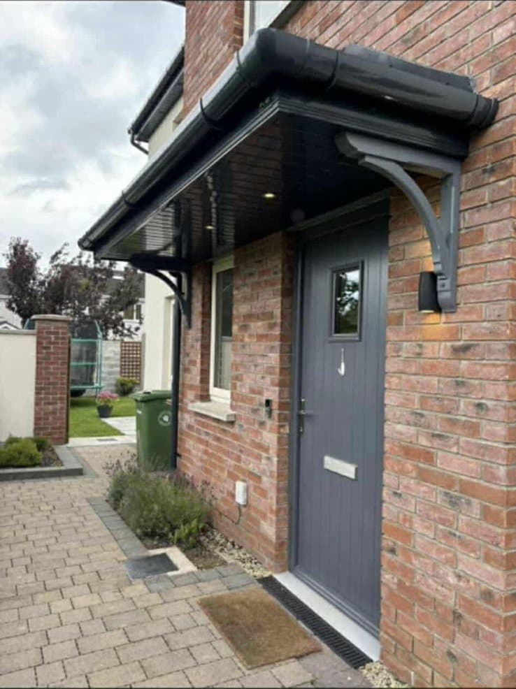 Grey lean-to door canopy with bracket supports on brick house
