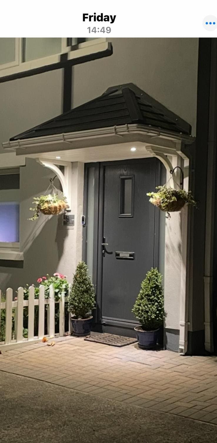 Hipped door canopy at night with hanging baskets and topiary plants